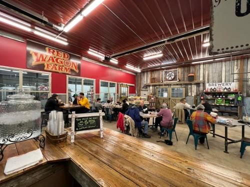 Interior of a rustic farm-themed café with patrons dining, a brewery sign, and a welcoming atmosphere.