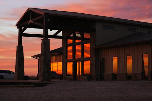 A modern building with large windows reflecting a vibrant sunset, surrounded by a gravel area.