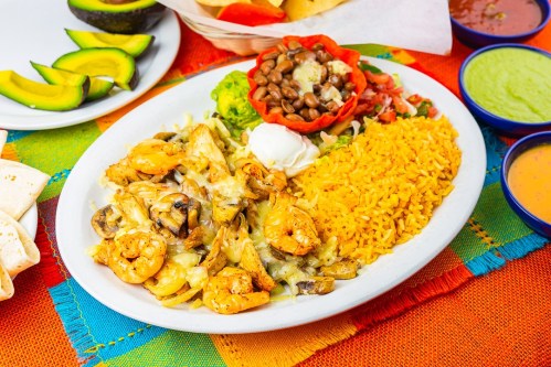 A colorful plate featuring shrimp, mushrooms, rice, beans, guacamole, and sour cream, with tortillas and avocado slices nearby.