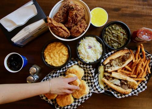 A spread of fried chicken, macaroni and cheese, coleslaw, green beans, fries, biscuits, and sandwiches on a wooden table.