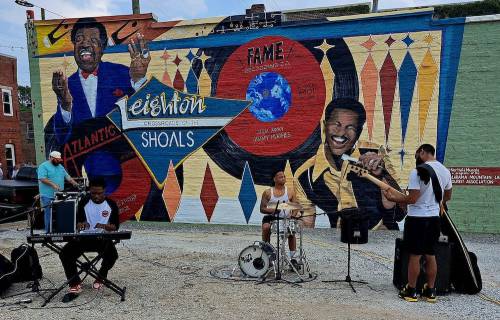 Musicians perform in front of a colorful mural celebrating Leighton Shoals and the Fame recording studio.