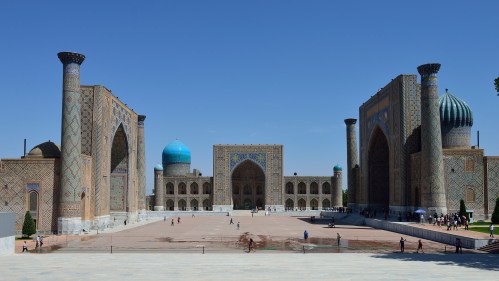 A panoramic view of the Registan Square in Samarkand, featuring ornate buildings and vibrant blue domes under a clear sky.
