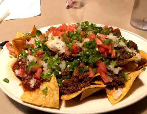 A plate of nachos topped with ground beef, diced tomatoes, onions, and green onions on a bed of tortilla chips.