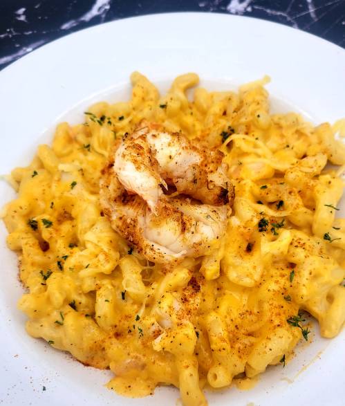 Creamy macaroni and cheese topped with a grilled shrimp, garnished with herbs and a sprinkle of paprika.