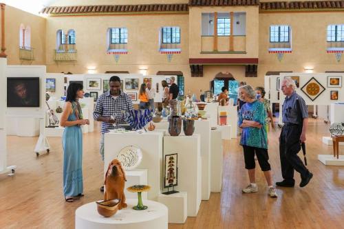 Visitors explore an art gallery filled with various sculptures and paintings, engaging in conversation and admiring the exhibits.