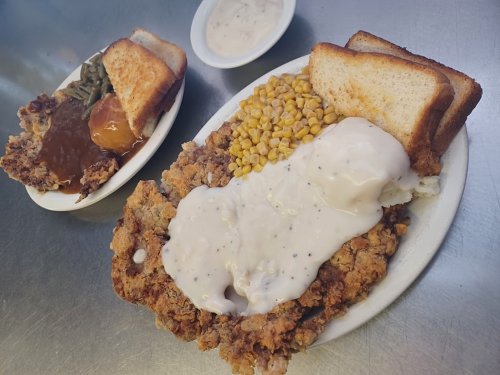 A plate of fried chicken with gravy, corn, and toast, alongside a bowl of greens and a dessert.