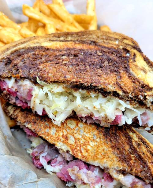 Close-up of a grilled sandwich filled with corned beef and sauerkraut, served with crispy French fries.