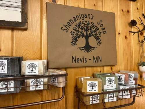 A wooden wall displays a sign for "Shenanigan's Soap" with various soap bars on shelves below.