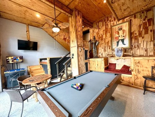 A cozy game room featuring a pool table, wooden decor, a small table, and a TV on the wall.