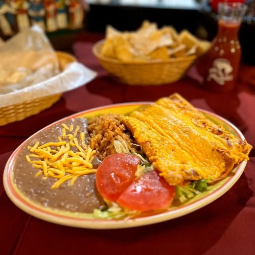 A colorful plate featuring enchiladas, refried beans, cheese, lettuce, and tomato, with tortilla chips in the background.