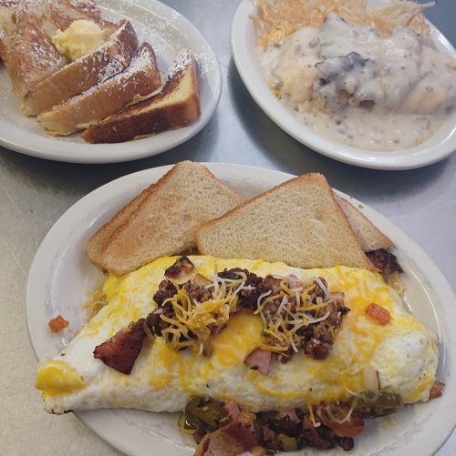 A hearty breakfast featuring a loaded omelet, toast, and a plate of biscuits and gravy.