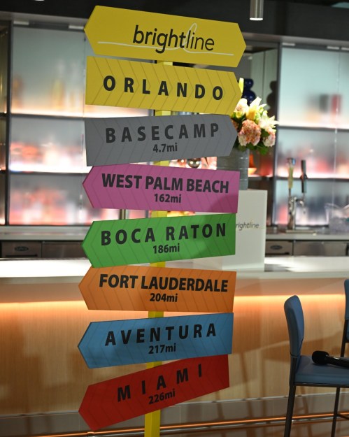 Colorful directional sign for Brightline train stations, listing distances to various locations in Florida.