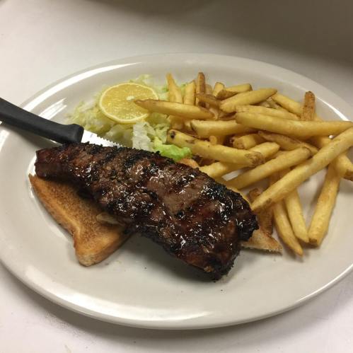 A plate with grilled steak on toast, served with lettuce, lemon, and a side of golden French fries.