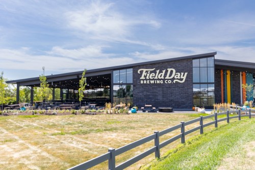 Exterior of Field Day Brewing Co. featuring a modern building with large windows and outdoor seating.