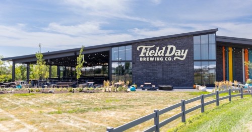 Exterior of Field Day Brewing Co. featuring large windows, a modern design, and outdoor seating in a grassy area.