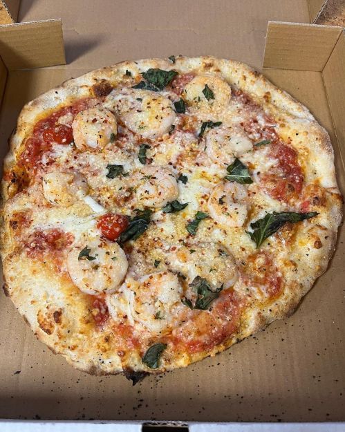 A freshly baked pizza topped with shrimp, cheese, and herbs, served in a cardboard box.