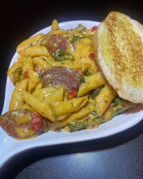 Creamy pasta with sausage, spinach, and red peppers, served with a slice of toasted bread on the side.