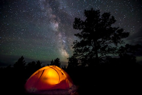A glowing orange tent under a starry night sky, with the Milky Way visible in the background.