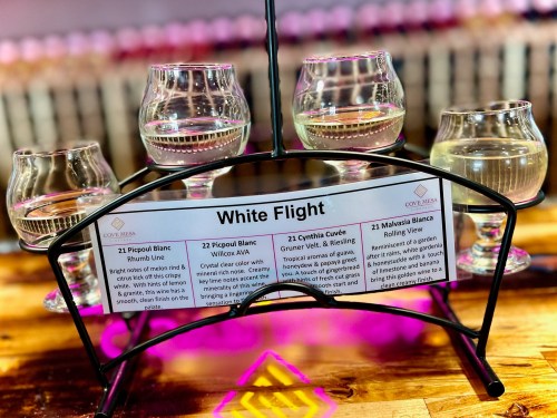 A wine flight display featuring four glasses of white wine, with a label detailing each wine's name and description.