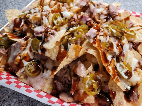 A close-up of a nacho platter topped with meat, jalapeños, onions, and drizzled with barbecue sauce and sour cream.