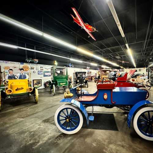 A vintage car museum featuring colorful antique cars and model airplanes hanging from the ceiling.