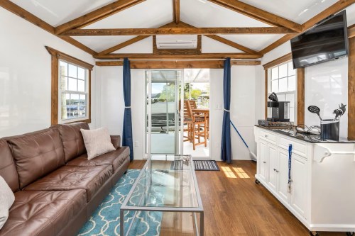 Cozy interior of a tiny house featuring a brown sofa, glass coffee table, and large windows with a view.