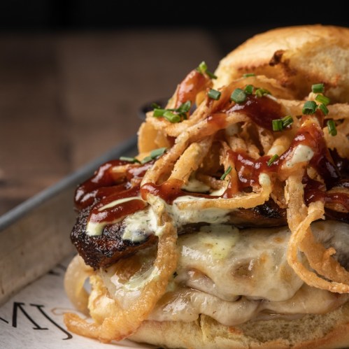 A close-up of a layered sandwich with melted cheese, crispy onions, and barbecue sauce on a toasted bun.