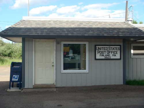 A small United States Post Office building in Finland, MN, featuring a door, window, and a blue mailbox outside.