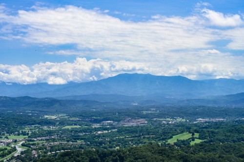 A panoramic view of lush green valleys and distant mountains under a partly cloudy sky.