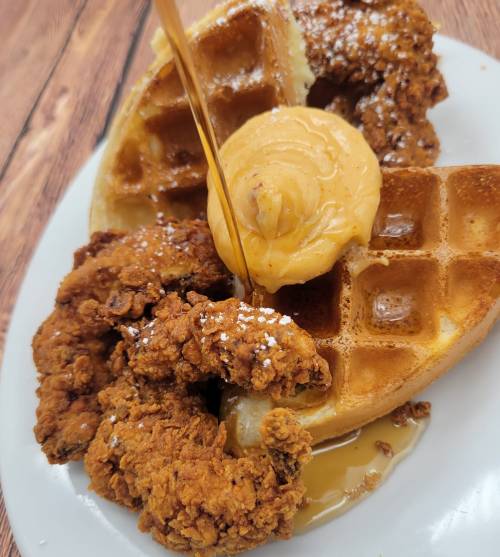 A plate featuring a waffle topped with butter and syrup, alongside crispy fried chicken pieces.