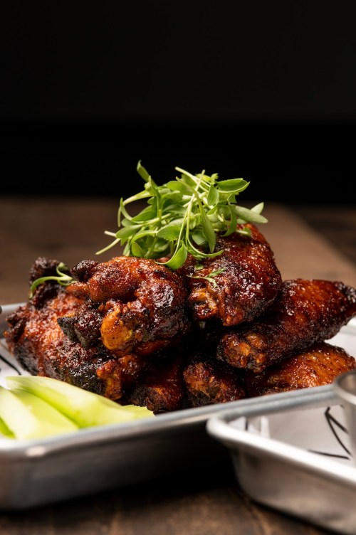 A plate of crispy chicken wings garnished with fresh greens, served with celery sticks on the side.