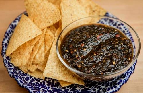 A blue and white plate filled with tortilla chips next to a bowl of dark salsa.