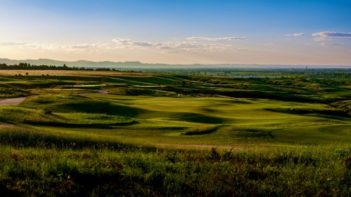 A scenic view of a lush green golf course under a clear blue sky, with rolling hills in the background.