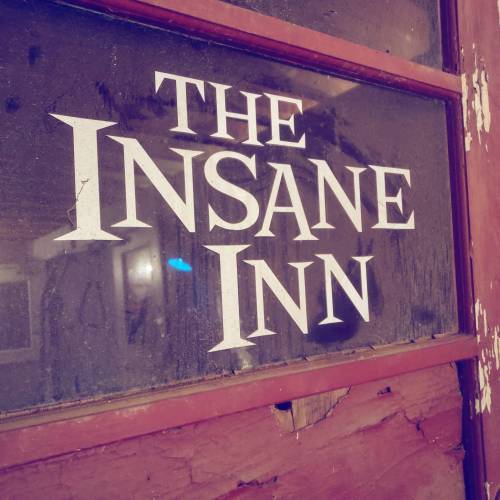 Sign on a window reading "The Insane Inn," with a rustic, weathered appearance.