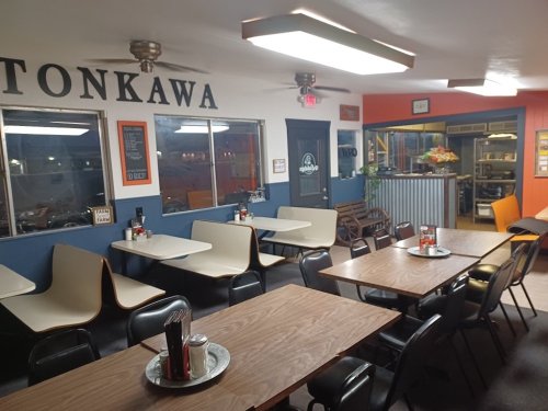Interior of a diner with wooden tables, chairs, and a sign reading "Tonkawa." Brightly lit with a cozy atmosphere.
