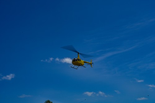 A yellow helicopter flying against a clear blue sky with a few scattered clouds.
