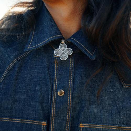 Close-up of a person's collar featuring a decorative pendant on a denim shirt.