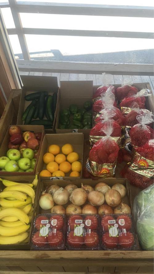A wooden display of assorted fruits and vegetables, including apples, bananas, cucumbers, and strawberries.