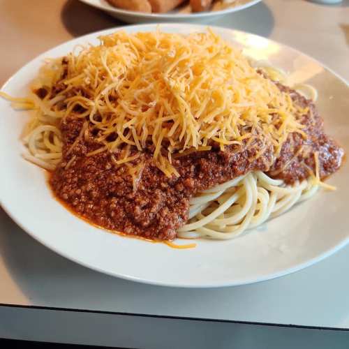 A plate of spaghetti topped with a hearty meat sauce and a generous layer of shredded cheese.