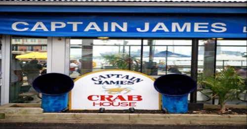 Sign for Captain James Crab House with blue accents and outdoor seating visible in the background.