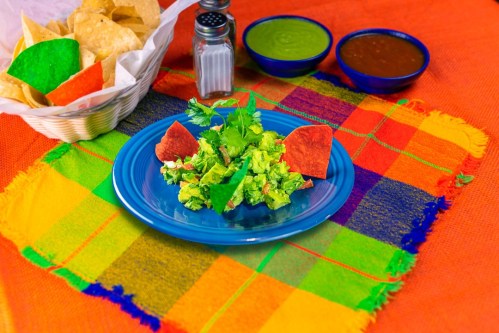 A vibrant plate of salad with tortilla chips, garnished with cilantro, on a colorful woven tablecloth.