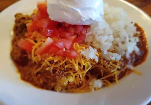 A plate of chili topped with shredded cheese, diced tomatoes, onions, and a dollop of sour cream.