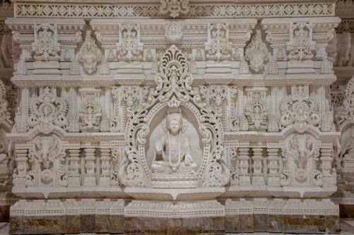 Intricate white stone carvings featuring a seated figure, surrounded by ornate floral and geometric designs.