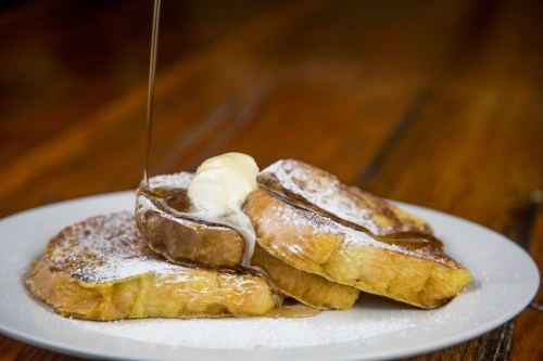 Three slices of French toast topped with butter and powdered sugar, drizzled with syrup on a white plate.
