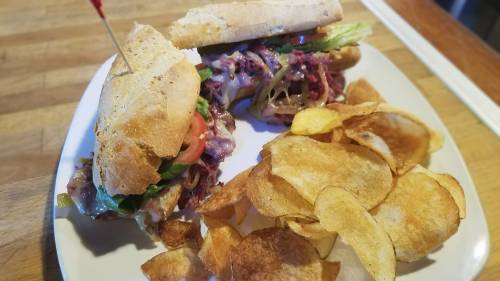 A sandwich with lettuce, tomato, and meat, served with a side of crispy potato chips on a white plate.