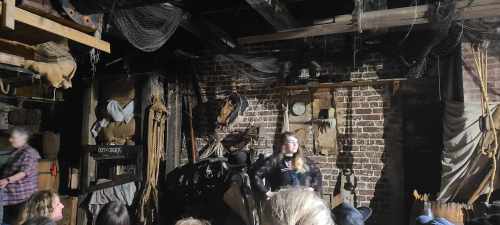 A dimly lit room with a performer on stage, surrounded by rustic decor and an audience in the foreground.