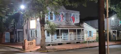 Historic building at night, featuring multiple flags and surrounded by trees, with a quiet street in the foreground.