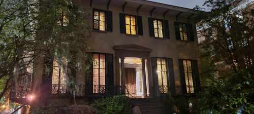 A two-story house at night, illuminated windows, surrounded by trees and shrubs, with a welcoming front entrance.