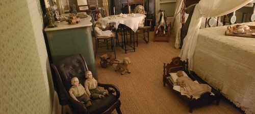 A vintage room with a bed, table, and dolls, creating a nostalgic and slightly eerie atmosphere.