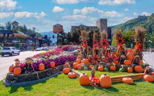 Colorful autumn display with pumpkins, flowers, and scarecrows along a busy street under a blue sky.